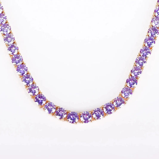 A close-up of a tennis-style necklace featuring round purple gemstones in a gold setting, photographed against a plain white background.