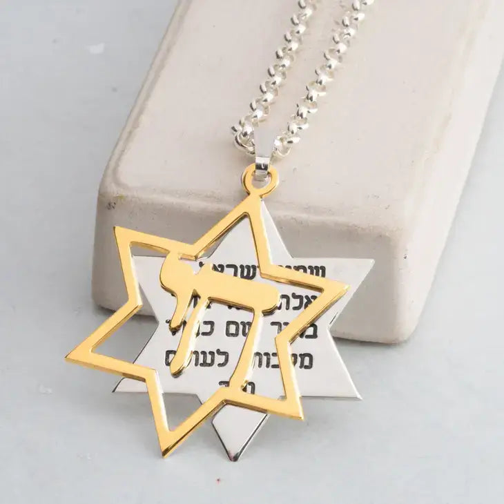 Gold and silver Star of David pendant necklace with a silver deer silhouette in the center, resting on a white Star of David card over a beige block.