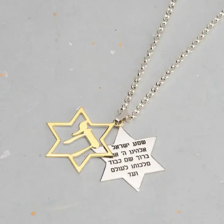 A silver ball-chain necklace with two Star of David pendants: one gold-tone outline pendant with a silhouette of a soccer player, and one silver-tone star pendant engraved with Hebrew text, shown on a light gray background.