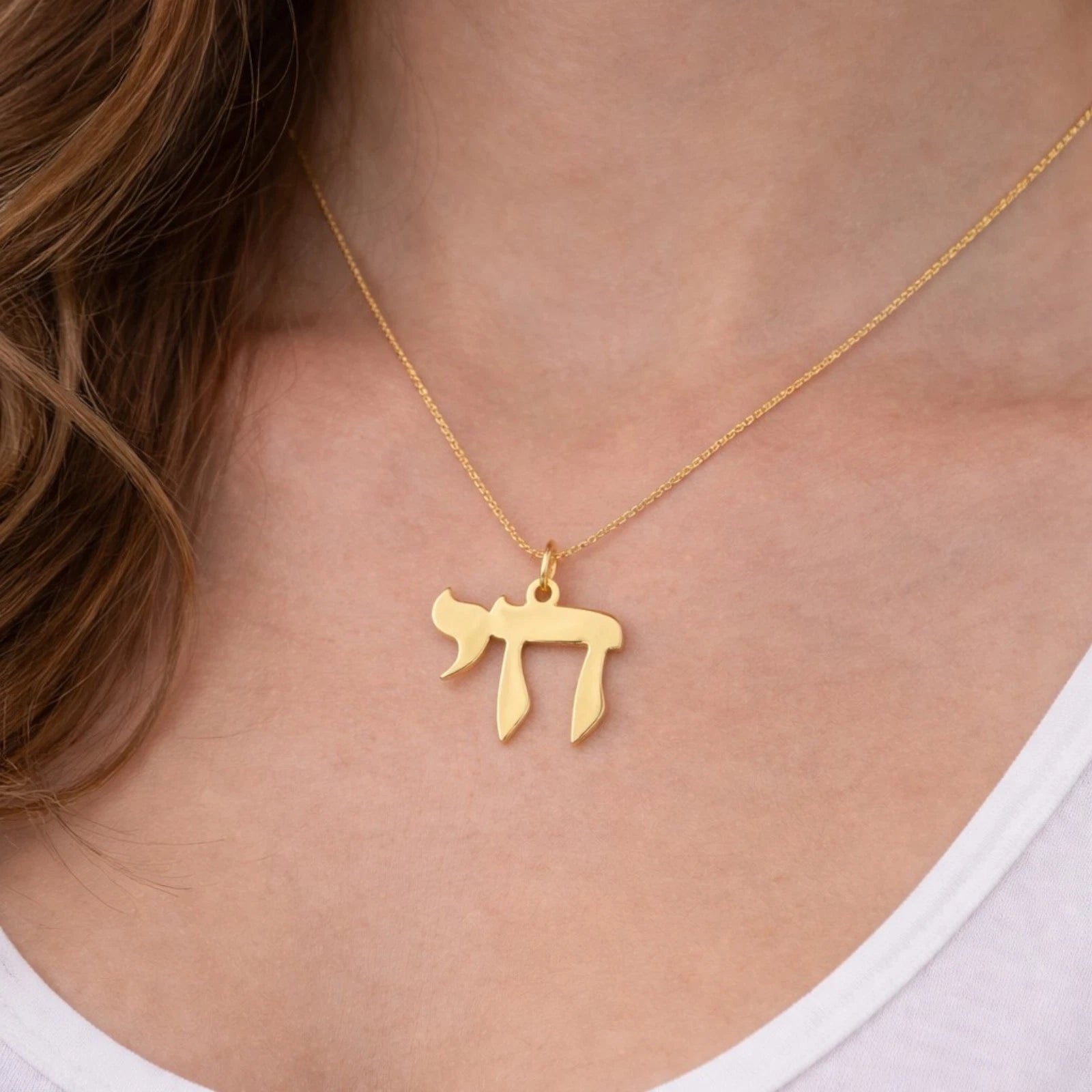 A gold necklace with a Hebrew letter pendant worn by a model, shown in a close-up shot of the neck and chest.